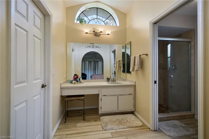 Ensuite bathroom with vanity, wood finished floors, a shower stall, and lofted ceiling