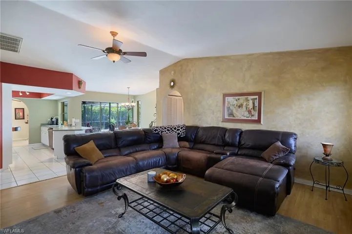 Living area with light wood-style floors, ceiling fan, a chandelier, and vaulted ceiling