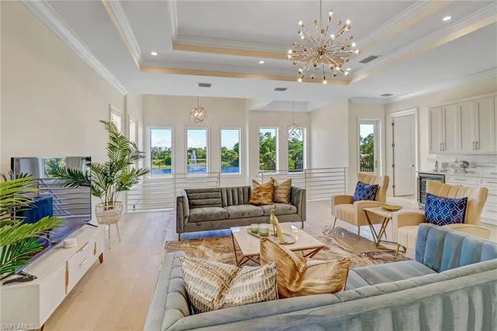 Living room with a tray ceiling, beverage cooler, crown molding, a notable chandelier, and light hardwood / wood-style floors