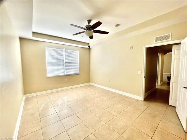 Tiled empty room featuring a tray ceiling and ceiling fan