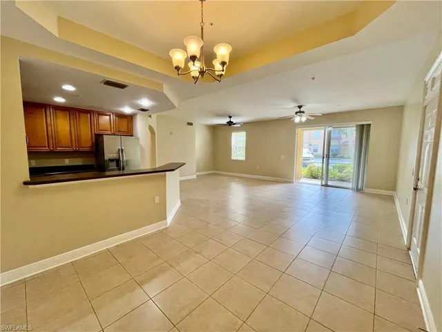 Kitchen with hanging light fixtures, light tile patterned flooring, ceiling fan with notable chandelier, a tray ceiling, and stainless steel fridge with ice dispenser