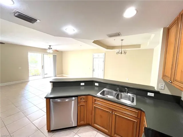 Kitchen featuring a raised ceiling, light tile patterned floors, sink, dishwasher, and ceiling fan with notable chandelier