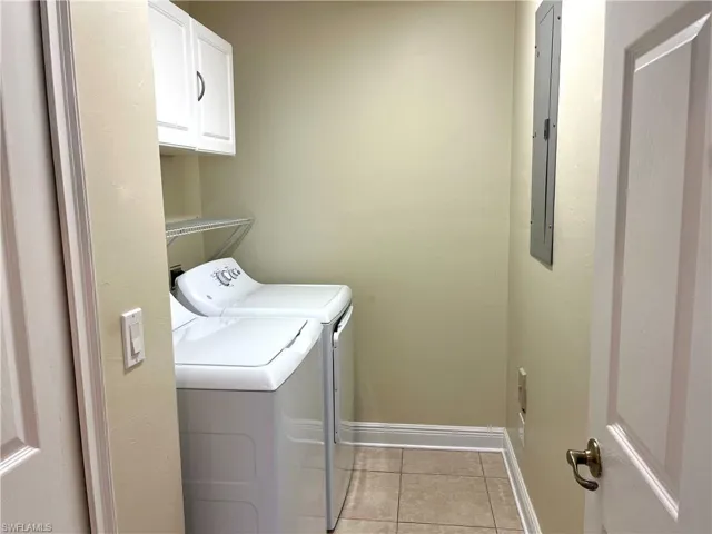 Washroom featuring washer and clothes dryer, light tile patterned floors, and cabinets