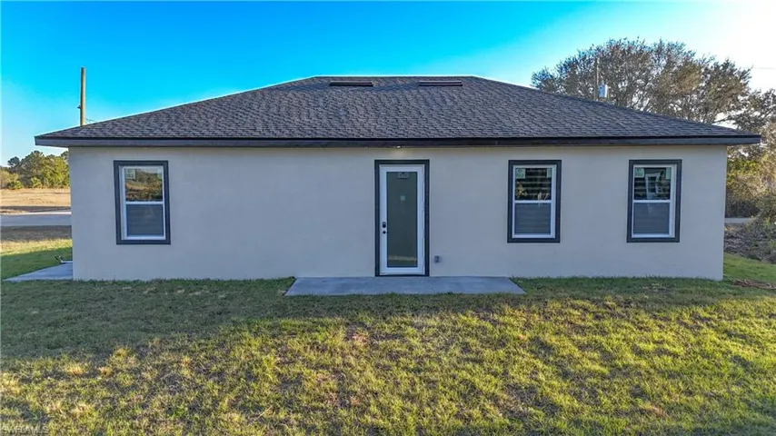 Rear view of property with roof with shingles, a lawn, a patio area, and stucco siding