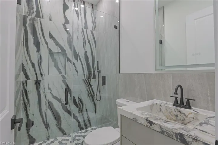 Full bath featuring a marble finish shower, vanity, and tile walls