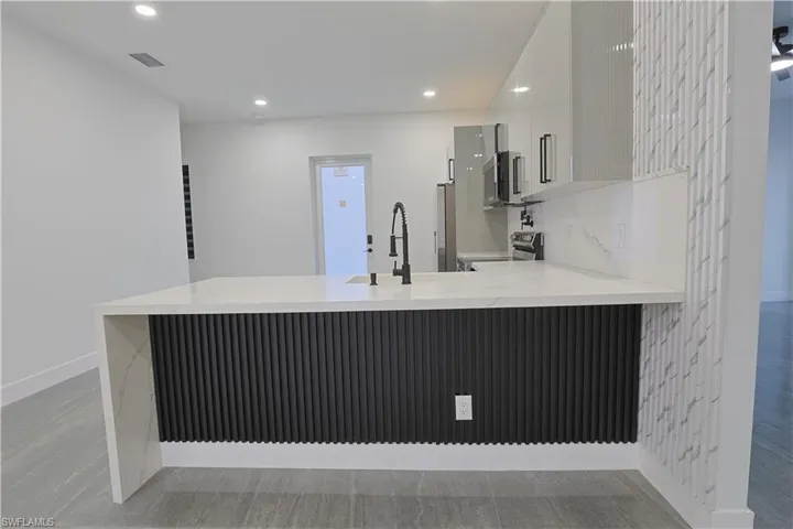 Kitchen with modern cabinets, a peninsula, white cabinetry, stainless steel appliances, and light stone countertops