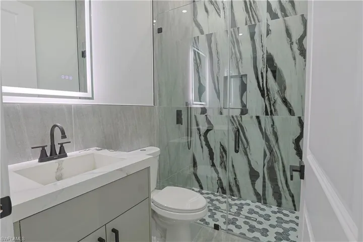 Full bathroom with vanity, a marble finish shower, tile walls, and a wainscoted wall