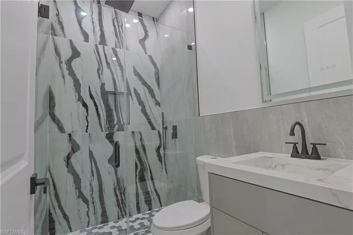 Bathroom with vanity, a marble finish shower, and tile walls