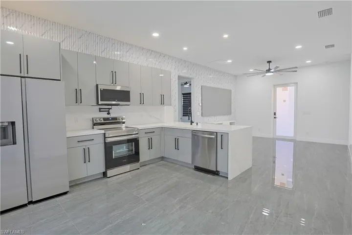 Kitchen featuring stainless steel appliances, a peninsula, recessed lighting, light stone countertops, and a ceiling fan
