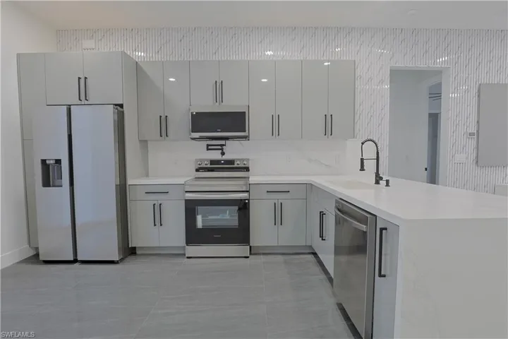 Kitchen featuring stainless steel appliances, gray cabinets, a peninsula, light stone countertops, and tasteful backsplash