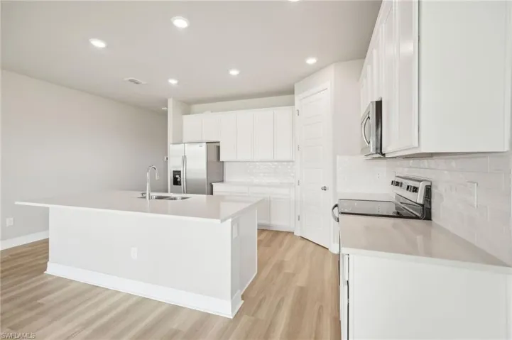 Kitchen featuring a center island with sink, light hardwood / wood-style floors, stainless steel appliances, and white cabinets