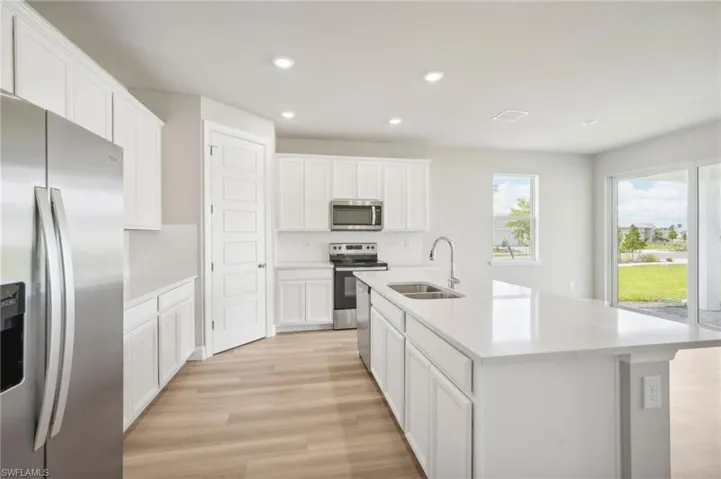 Kitchen featuring light hardwood / wood-style floors, sink, an island with sink, white cabinets, and stainless steel appliances