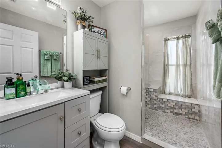 Bathroom featuring vanity, tiled shower, wood-type flooring, and toilet