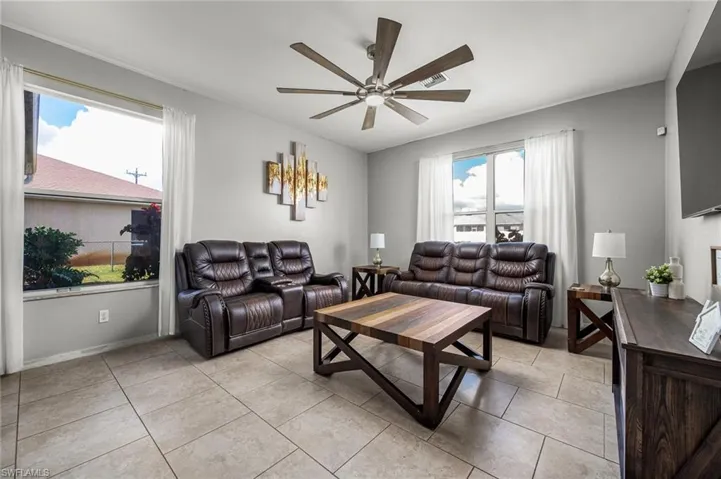 Living room with light tile patterned floors, a healthy amount of sunlight, and ceiling fan