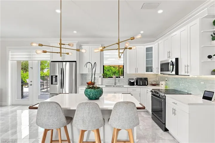 White shaker cabinetry, stainless steel appliances, a light-toned backsplash, a central kitchen island with seating, and large-format tile flooring