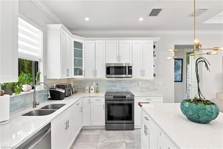 White cabinetry with brushed nickel hardware, stainless steel appliances, light-toned backsplash, light-toned countertops, and recessed lighting