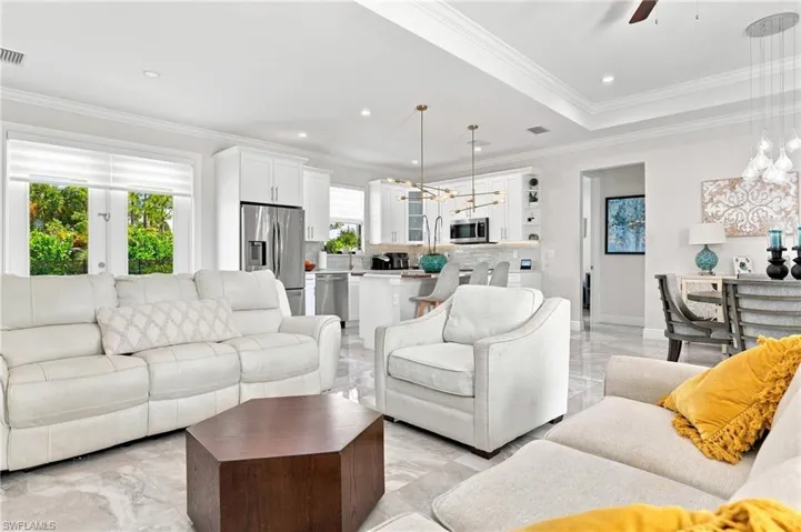 Open-concept living area with tray ceilings, recessed lighting, and large format tile flooring