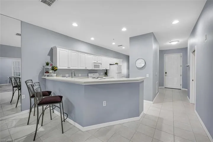 Kitchen with white cabinetry, light countertops, visible vents, and white appliances