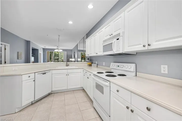 Kitchen featuring light countertops, a sink, a peninsula, light tile patterned floors, and white appliances
