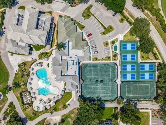 Expansive resort-style swimming pool, surrounding sun deck with multiple umbrellas, multiple hard tennis courts, multiple hard pickleball courts, and a large paved parking area