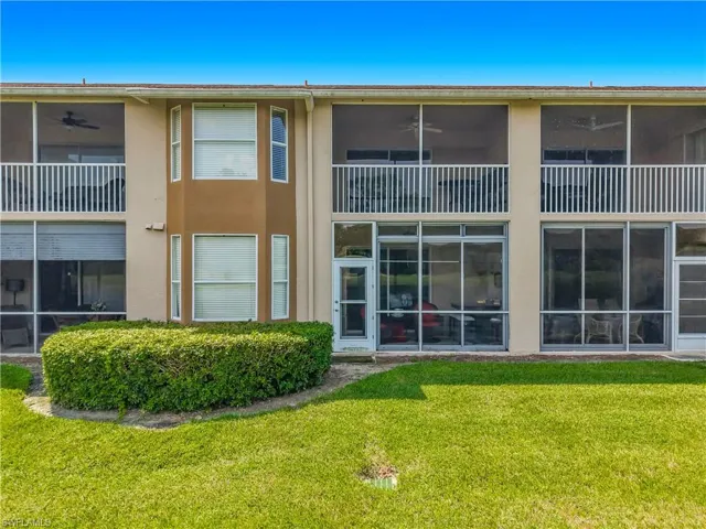 Two-story exterior with screened upper and lower balconies, a bay window feature, and a well-maintained lawn with manicured shrubbery