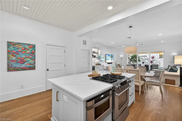 Kitchen with stainless steel range with gas cooktop, a kitchen island, decorative light fixtures, dark wood-type flooring, and open floor plan