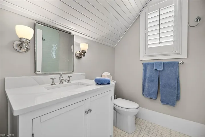 En-suite guest bathroom with vanity, vaulted ceiling, light tile patterned flooring, and tiled shower