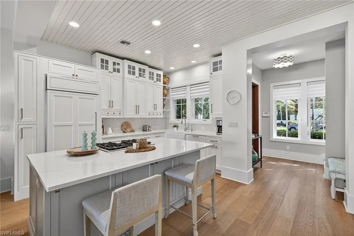 Kitchen with wood ceiling, glass insert cabinets, a breakfast bar, light stone countertops, and light wood-type flooring