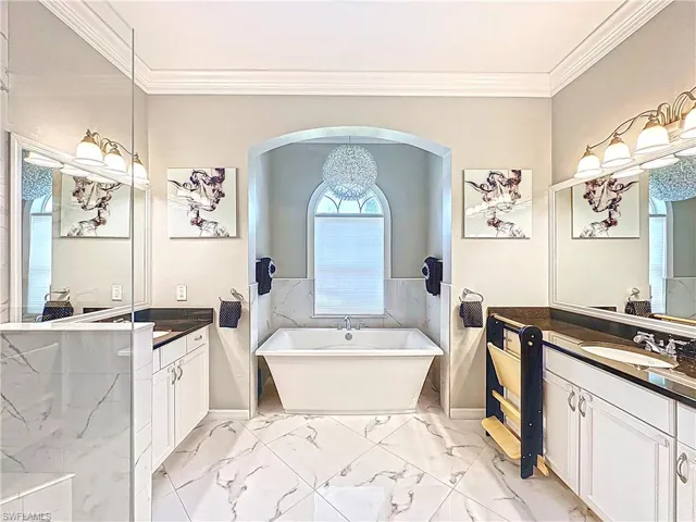 Bathroom featuring a soaking tub, two vanities, ornamental molding, and marble finish flooring
