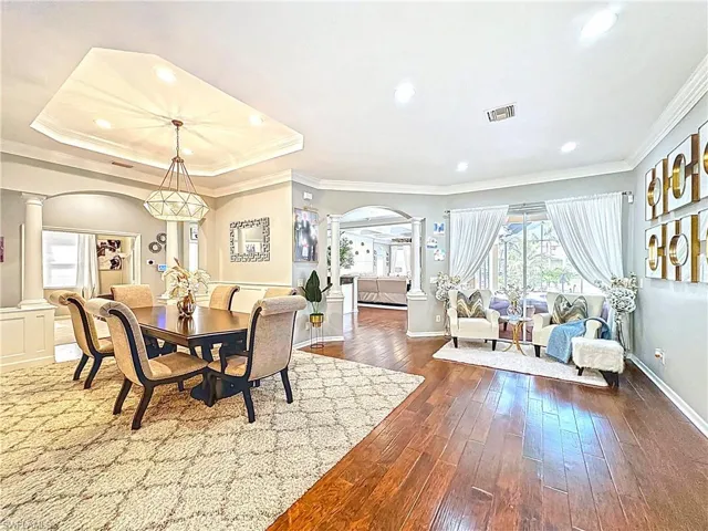 Dining space with decorative columns, arched walkways, dark wood-style floors, recessed lighting, and ornamental molding