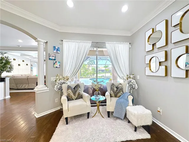 Living area featuring ornate columns, arched walkways, wood finished floors, ornamental molding, and recessed lighting