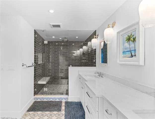 Spacious bathroom featuring a glass-enclosed shower with dark subway tile, a built-in shower bench, and a dual vanity with white countertops and undermount sinks