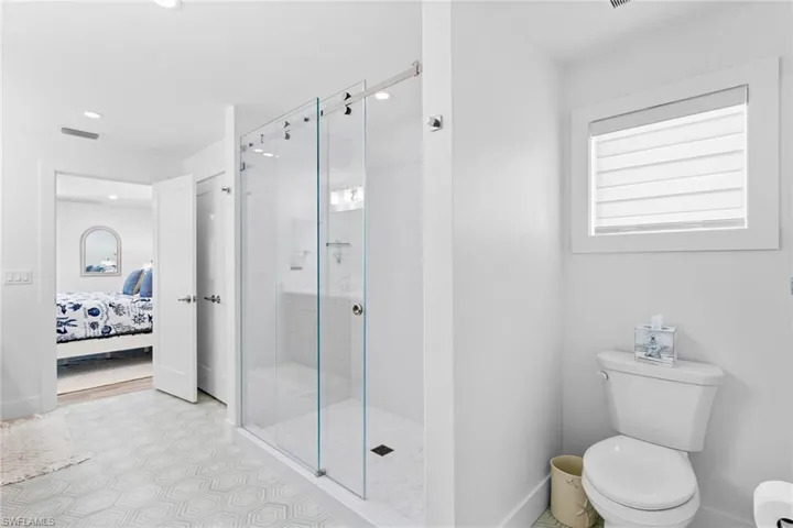 Bathroom featuring a glass-enclosed shower with sliding doors, a white toilet, and a window with privacy blinds