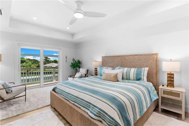 Bright room with tray ceiling and recessed lighting, featuring sliding glass doors opening to a balcony with water frontage