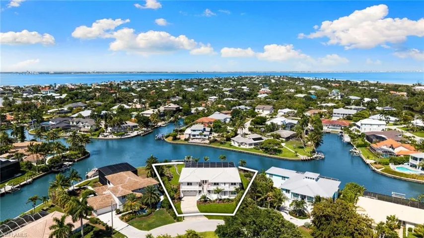 Waterfront property featuring a white multi-story exterior, an attached garage, a paved driveway, mature landscaping, and solar panels