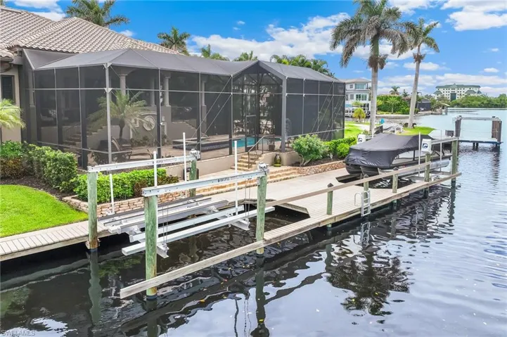 Dock area with boat lift, a water view, glass enclosure, an outdoor pool, and a sunroom