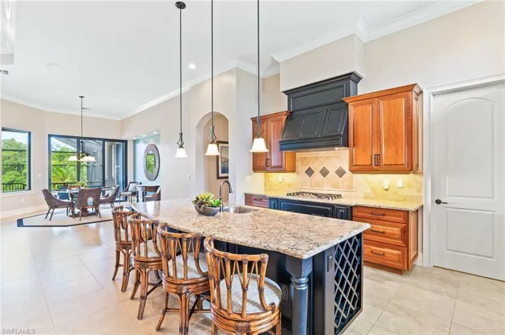Kitchen with ornamental molding, tasteful backsplash, a kitchen breakfast bar, light stone counters, and hanging light fixtures