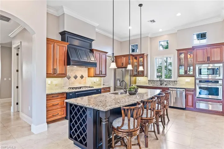 Kitchen featuring crown molding, tasteful backsplash, hanging light fixtures, glass insert cabinets, and arched walkways