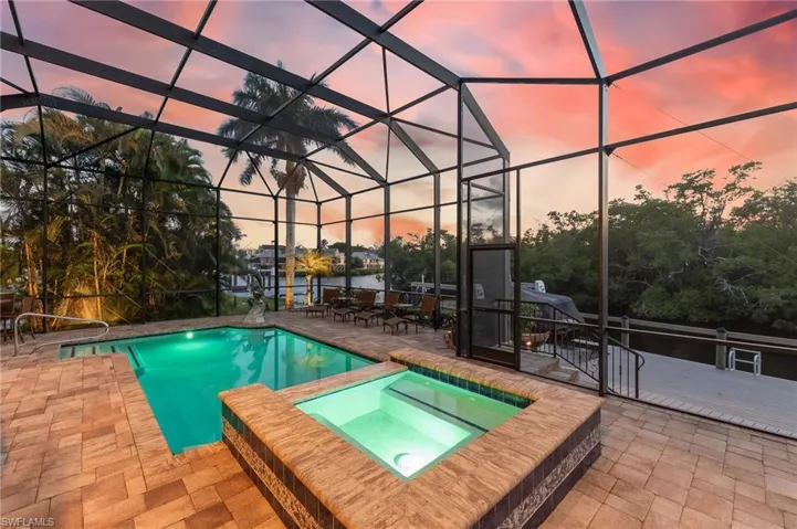 Pool at dusk featuring a water view, a lanai, a sunroom, a pool with connected hot tub, and a patio area
