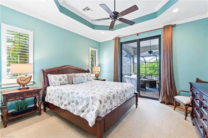 Carpeted bedroom with a tray ceiling, multiple windows, ornamental molding, access to exterior, and recessed lighting