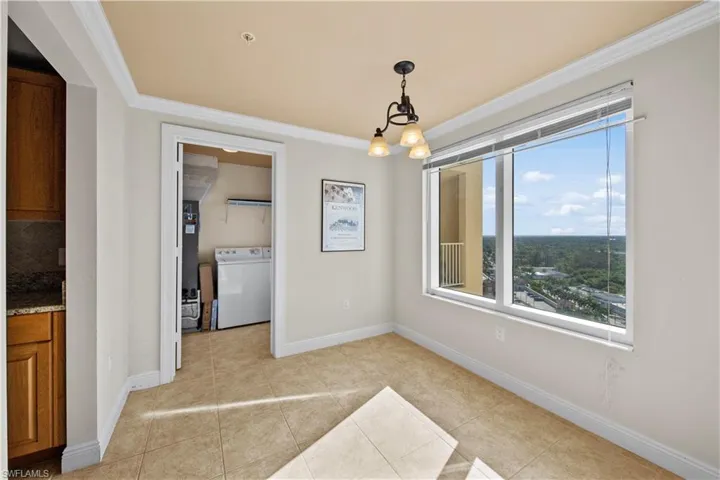 Unfurnished dining area with ornamental molding, an inviting chandelier, washer / dryer, and light tile floors
