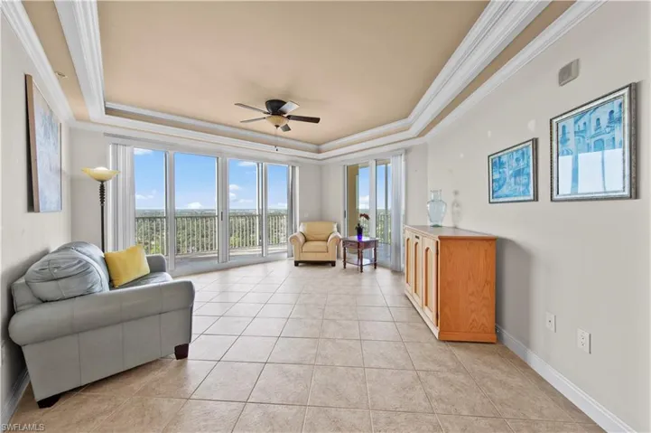 Living room with ceiling fan, ornamental molding, light tile flooring, and a raised ceiling