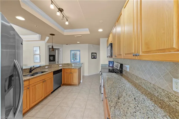 Kitchen featuring light stone countertops, crown molding, a raised ceiling, sink, and appliances with stainless steel finishes