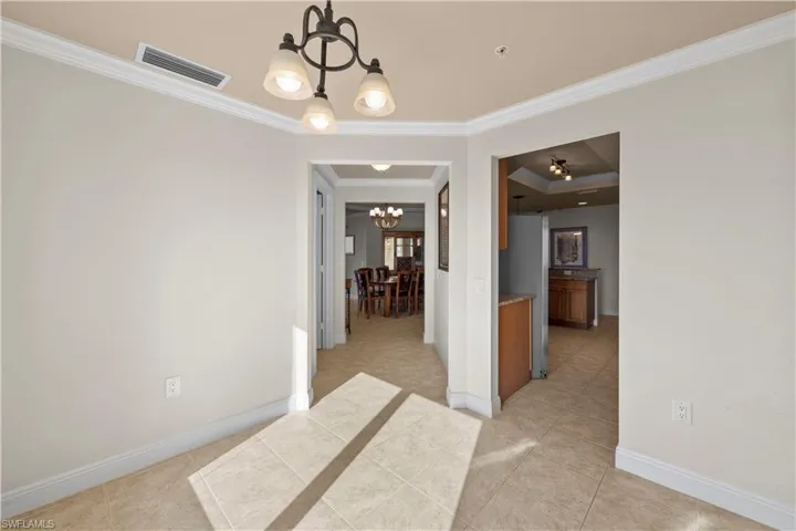 Dining space featuring a notable chandelier, a raised ceiling, light tile flooring, and ornamental molding
