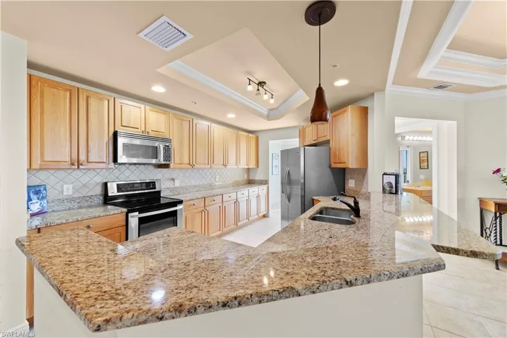 Kitchen featuring stainless steel appliances, a tray ceiling, kitchen peninsula, decorative light fixtures, and sink