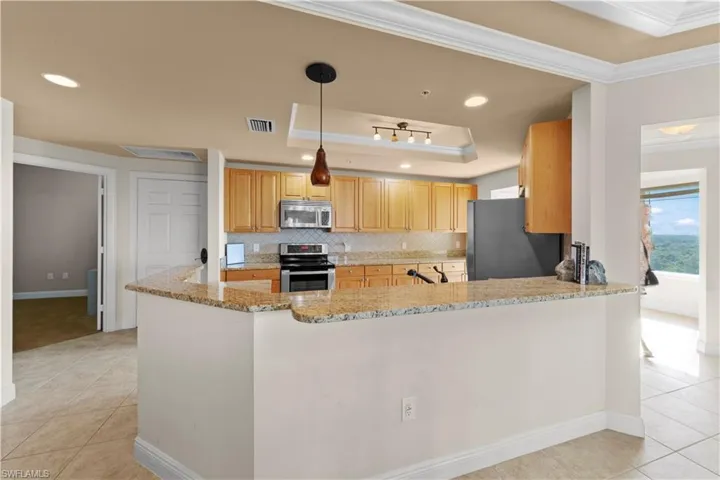 Kitchen with stainless steel appliances, light tile floors, a raised ceiling, and kitchen peninsula