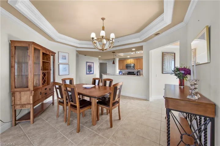 Tiled dining area with a tray ceiling, crown molding, and a chandelier