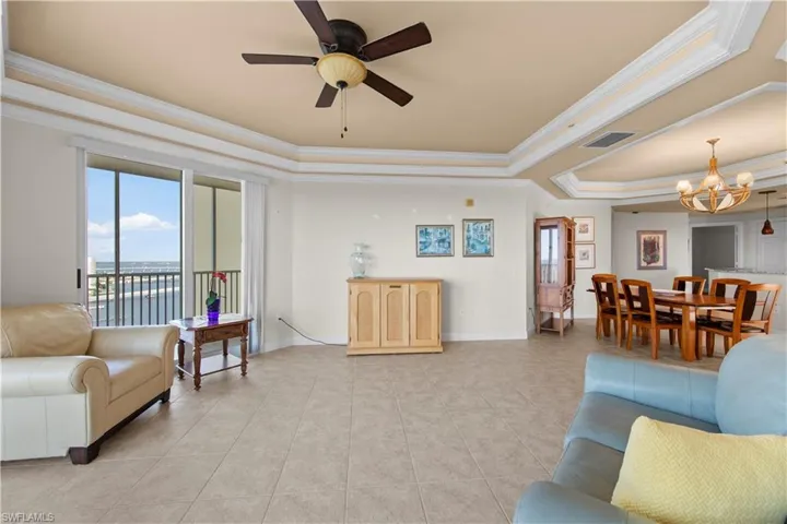 Tiled living room featuring a tray ceiling, crown molding, and ceiling fan with notable chandelier