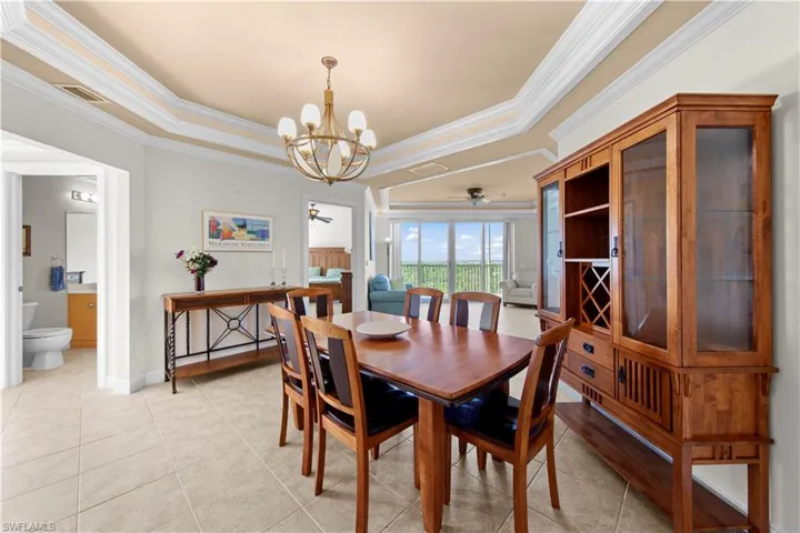 Dining room featuring light tile floors, a tray ceiling, crown molding, and ceiling fan with notable chandelier