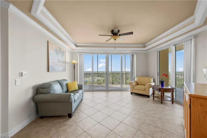Living room with ceiling fan, a tray ceiling, light tile floors, and crown molding